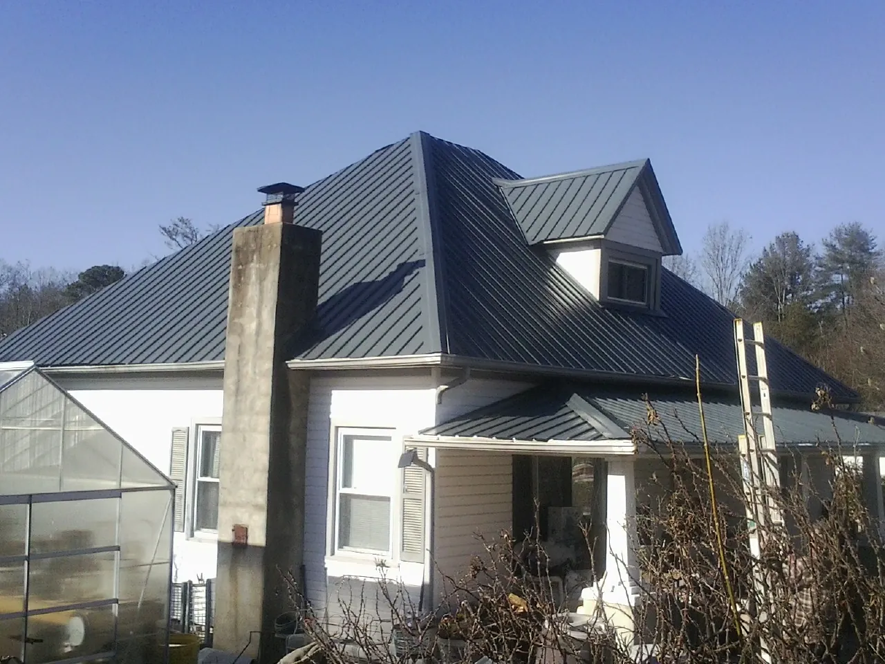 Dark blue standing seam metal roof on a white farmhouse with dormer — Slate & Tile Roof Repair by Roofing Brothers in Turon