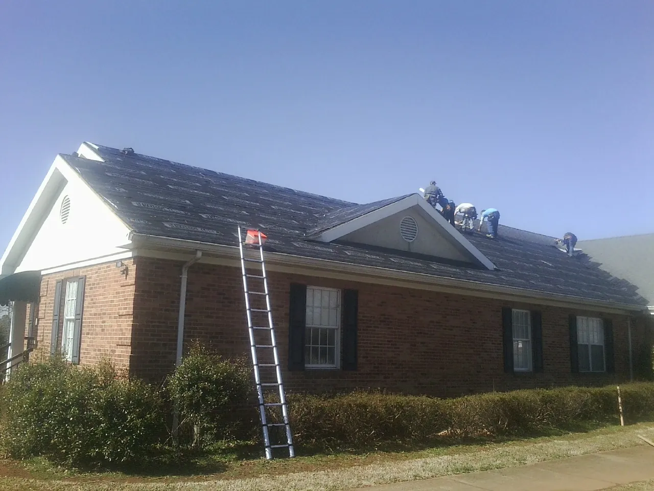 Crew tearing shingles off a brick ranch roof with a ladder set — Metal Roof Repair work by our crew in Turon