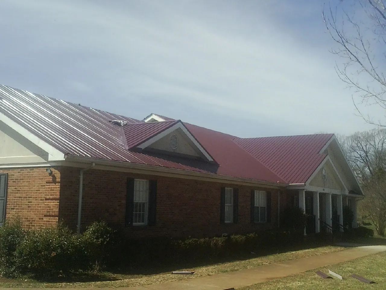 Red metal roof with gabled entries on a long brick building, from a Hail Damage Roof Repair job in Turon