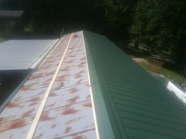 Old rusted panels beside newly installed green metal roofing — Wind Damage Roof Repair by Roofing Brothers in Turon