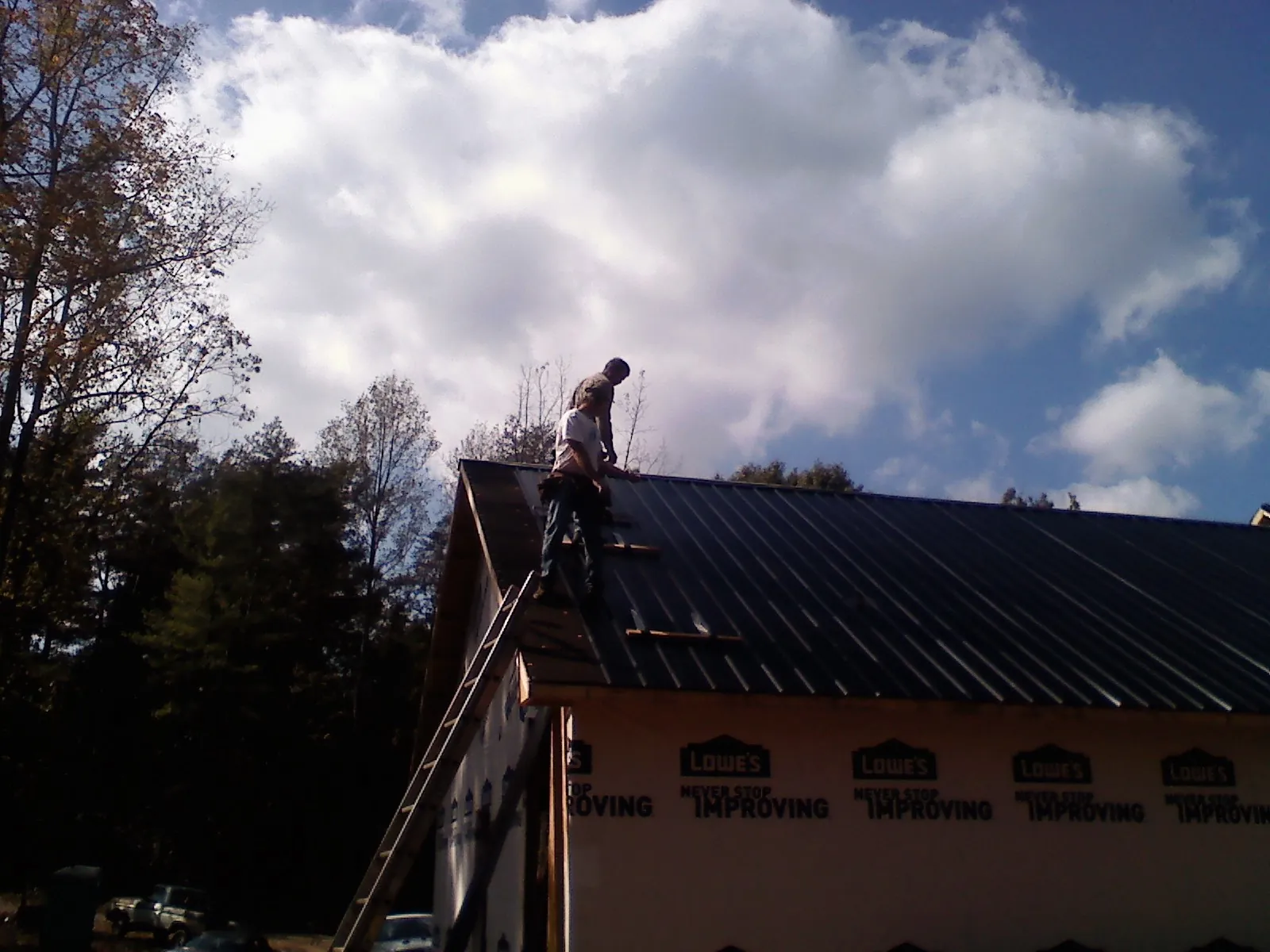 Roofer fastening dark metal panels high against a cloudy sky, from a Roof Inspection job in Turon