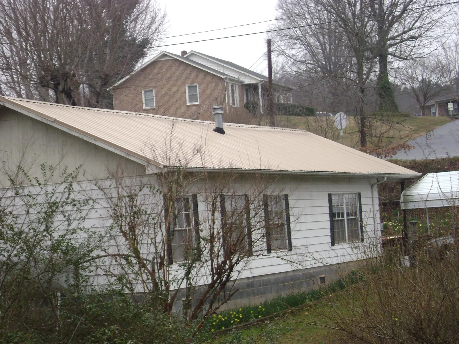 Tan metal roof on a white sided house set into a hillside — Commercial Roofing by Roofing Brothers in Turon